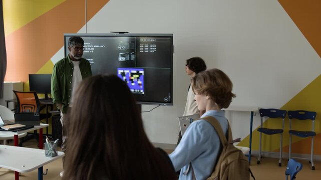 Teenagers entering modern classroom and teenage boy shaking hands with middle-aged Indian teacher in front of interactive screen. Clip is ideal for promoting STEM education and coding bootcamps