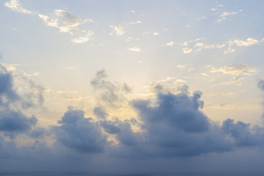 Soft sunlight and crepuscular rays filtering through dark, fluffy cumulus clouds above a serene ocean horizon in Gran Alacant, Alicante, Spain. Peaceful summer sky landscape background