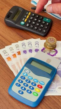 Vertical video social media &ndash; Closeup of a man&rsquo;s hand using a calculator behind British sterling pound currency notes and coins, plus a bank card inside an internet transactions reader.