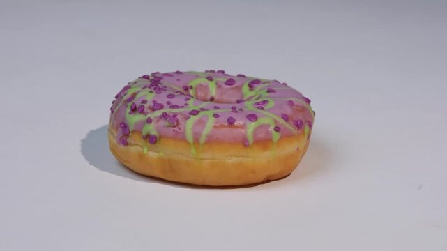 Pink donut with green and purple sprinkles sits on white background, side view, donut spinning