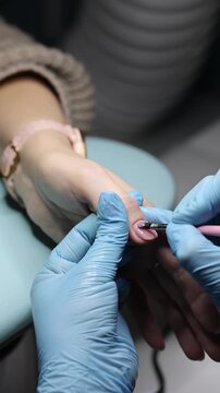 Nail master in rubber gloves makes professional manicure to girl in beauty salon	. Vertical video