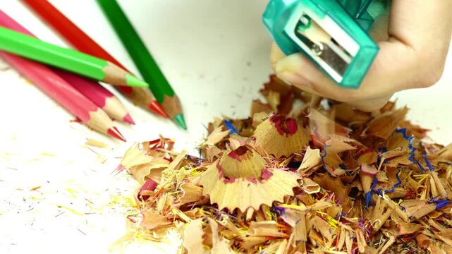 Color pencil sharpening with manual sharpener front view close up creating wooden spiral shavings in 4K Ultra HD footage.
