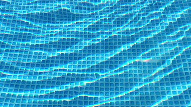 High angle view of clear blue water caustics and sunlight reflections rippling over a blue mosaic tiled swimming pool floor. Summer background.