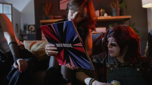 Young adults with alternative style sitting on sofa, examining rock music vinyl record sleeve. Clip is ideal for music store ads or youth culture campaigns