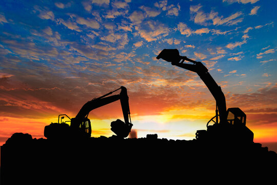 Two Crawler excavators silhouette are digging the soil in the construction site on   sunset clouds  sky background .