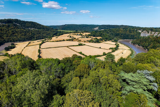 Parched agricultural fields inside a river bend, dry stubble pastures surrounded by woodland and limestone cliffs under a bright blue sky, elevated wide view