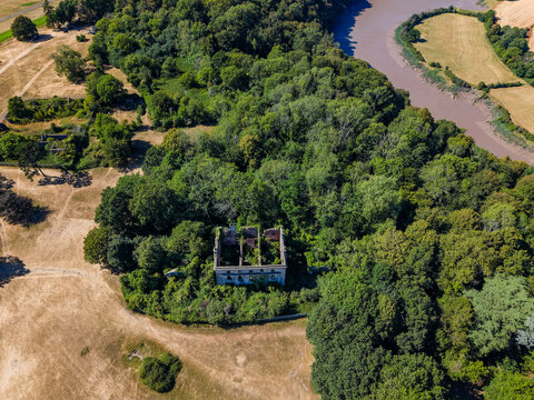 Aerial view of Piercefield House ruins in Chepstow, Wales, roofless 18th century mansion shell overgrown with vegetation near the winding River Wye, wide shot