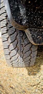Close-up of a rugged off-road SUV with deep-tread tires on an unpaved sandy trail and gravel road; four-wheel-drive vehicle equipment for outdoor adventures in the desert