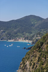 Fototapeta premium Passenger ferries at Monterosso al Mare, Italy show mountain and cliff scale around distant bay from high telephoto coastal perspective.