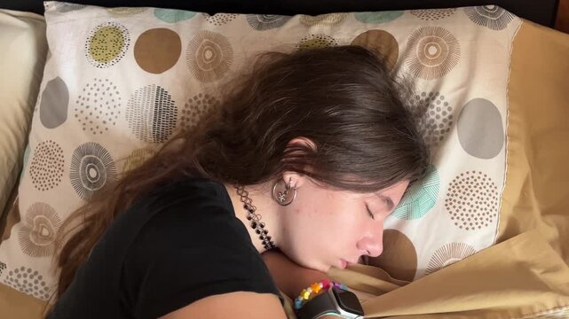  Serene teenager with long brunette hair peacefully sleeping in her bed. She is resting under the covers in a comfortable position, highlighting tranquility and relaxation.