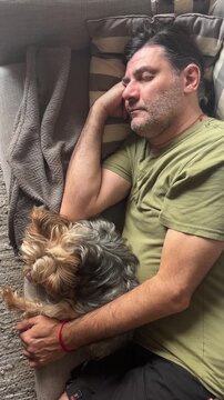 Mature man peacefully sleeping on the couch while cuddling his adorable yorkshire terrier, embracing tranquility and the strong bond between pet and owner in a cozy home setting