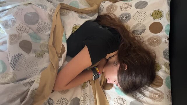 Young woman with long dark hair peacefully sleeping in her bed, deeply breathing and dreaming while resting in a comfortable position under the cozy blankets