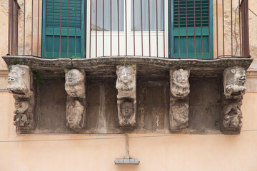 Modica, Italy  1st August 2026: Baroque architectural detail with carved grotesque face and ornate stonework on a balcony in Sicily. © Leckerstudio