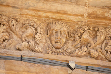 Modica, Italy  1st August 2026: Baroque architectural detail with carved grotesque face and ornate stonework on a balcony in Sicily. © Leckerstudio