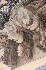 Modica, Italy  1st August 2026: Baroque architectural detail with carved grotesque face and ornate stonework on a balcony in Sicily. © Leckerstudio
