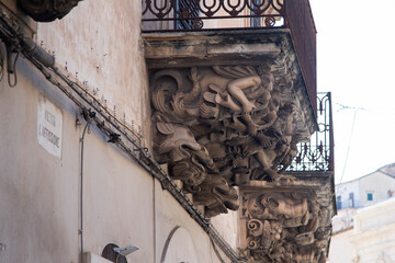 Modica, Italy  1st August 2026: Baroque architectural detail with carved grotesque face and ornate stonework on a balcony in Sicily. © Leckerstudio