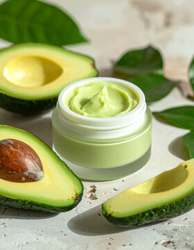 Nourishing avocado face cream in modern cosmetic jar, fresh avocado halves and slices, green leaves, natural stone surface, healthy moisturizing skincare concept, beauty product. Close-up.