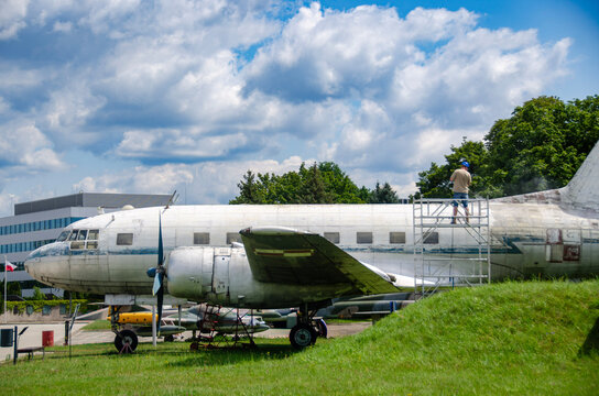 Worker pressure washing the weathered fuselage of a retired aircraft from a scaffold. Aircraft restoration worker cleaning an old airplane exterior with a high pressure washer. Maintenance technicia
