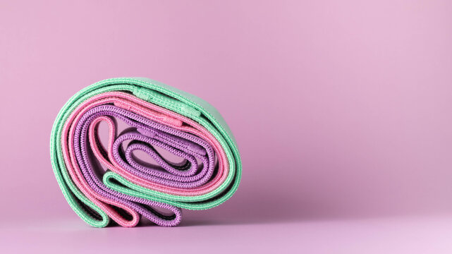 Fabric, elastic resistance bands, rolled up, three colors, green, pink and purple, room for text.