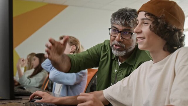 Indian middle aged male teacher explaining computer task to Caucasian teenager in classroom. Video is perfect for marketing coding bootcamps, school technology programs, and modern education
