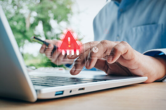 Business professional typing on laptop computer keyboard, Holographic red warning and error exclamation mark icons, Smartphone monitoring, cybersecurity threat concept, risk management, system failure