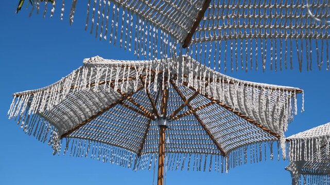 White macrame beach umbrella with fringe against clear blue sky at summer resort