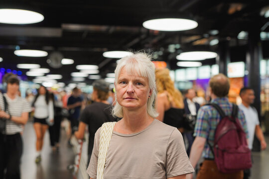 Senior woman looking at camera at subway with blurred people walking in background - Busy city metro, travel and elderly person concept