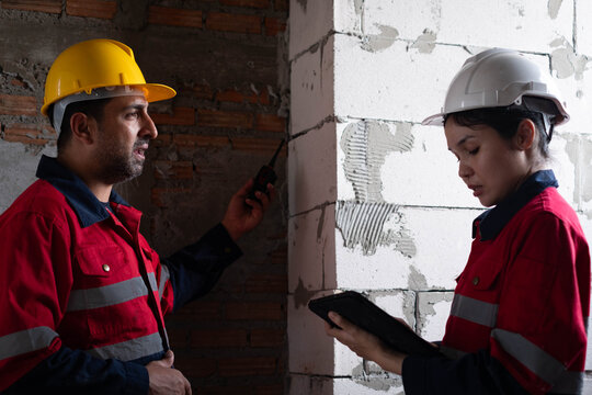 Construction engineers reviewing inspection data at an unfinished building, coordinating structural quality, safety compliance, project progress using digital technology for residential construction.