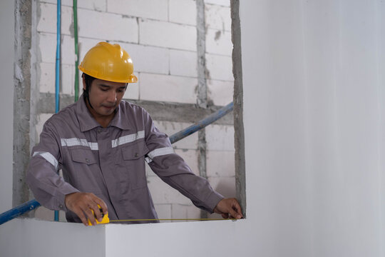 Construction worker measuring an unfinished interior wall with a tape measure, highlighting precision, building inspection, renovation, safety, craftsmanship, planning, and professional work.