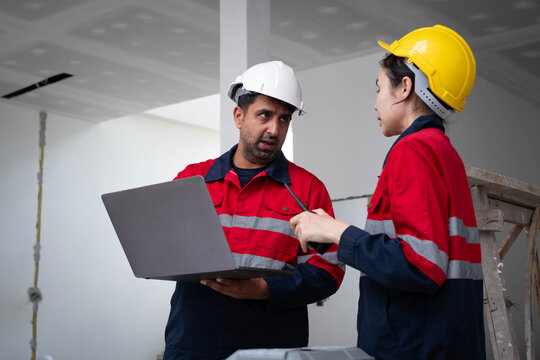 Construction workers in hardhats discuss a project while reviewing a laptop and using a radio at a worksite, showing teamwork, engineering, safety, communication, planning, and field management.