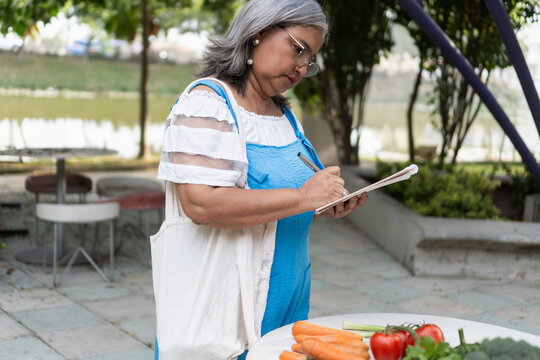 Mature woman writing grocery list with carrots outside