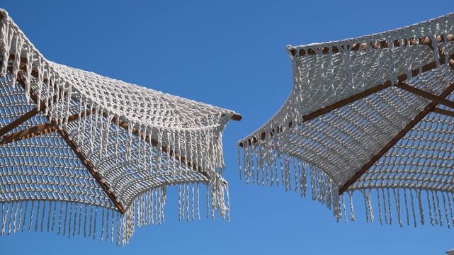 White macrame beach umbrellas against a clear blue sky on a sunny day