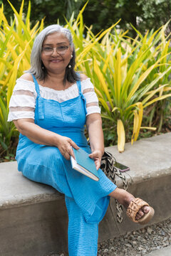 Senior woman smiling sitting outdoors holding book