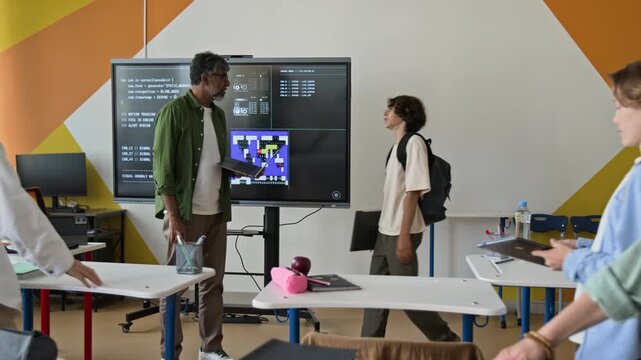 Middle aged South Asian teacher holding laptop and talking to teenage student in coding classroom. Clip is ideal for marketing STEM education, computer science, or high school technology courses