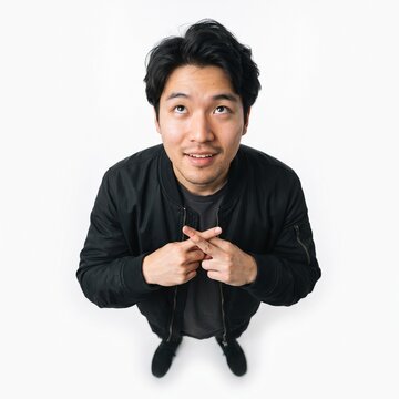 Young Asian man looking up with fingers crossed and a hopeful expression on white background