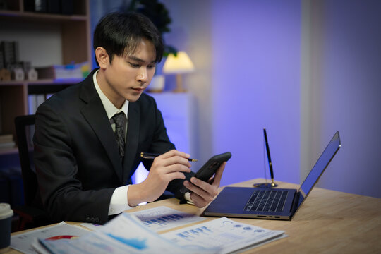 Asian Businessman Working Late Night in Office, Serious Executive Reading Financial Paperwork and Analyzing Reports at Desk