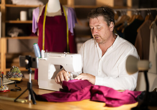 Man seamstress operating by sewing machine, manufactures clothing