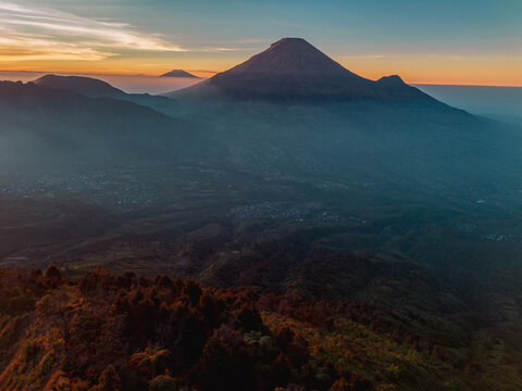 A panoramic view of Mount Sindoro set against a golden-blue sky at sunrise. Rising over 3,000 meters above sea level, the mountain looks majestic and beautiful on a clear morning.