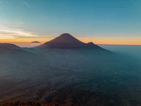 A panoramic view of Mount Sindoro set against a golden-blue sky at sunrise. Rising over 3,000 meters above sea level, the mountain looks majestic and beautiful on a clear morning.