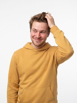 Young man with blond hair and beard wearing a yellow hoodie scratching his head and smiling
