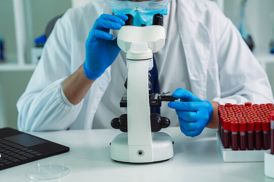 Scientist Holding Blood Sample Test Tube with Microscope and Rack of Blood Vials in Medical Laboratory