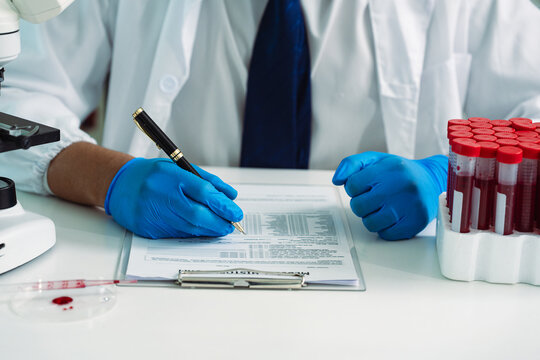 Scientist Holding Blood Sample Test Tube with Microscope and Rack of Blood Vials in Medical Laboratory