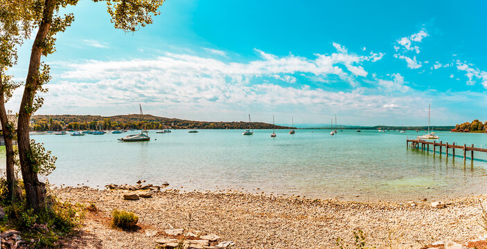 sunny day at Lake Ammersee in Bavaria, Germany, Europe.  long wooden pier creating a classic lakeside viewpoint. sailboats and yachts are anchored across the calm lake under bright sky