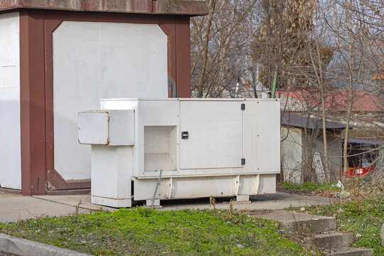 Old Diesel Generator Set in Big White Box Behind Industrial Building