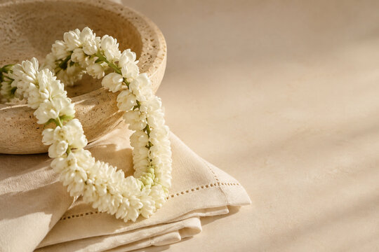 Sampaguita garland draped over travertine bowl with linen napkin, still life concept