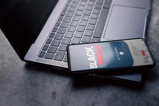 Black Friday sale banner on smartphone next to laptop keyboard. Phone screen showing Black Friday offer.