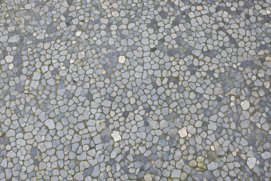 Natural pebble stone floor texture featuring densely arranged small stones in soft grey, beige, and muted earthy tones, creating an organic surface for patios, pathways, courtyards, and architecture.