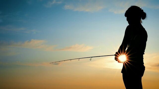 Silhouette of a woman holding a fishing rod against a sunset sky