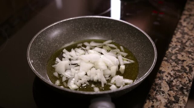Pouring chopped onion into pan with hot olive oil. Woman pouring fresh cut onion into pan.