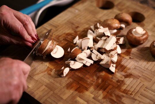 Slicing portobello mushrooms with knife on wooden cutting board. Woman chopping fresh portobello mushrooms with knife.